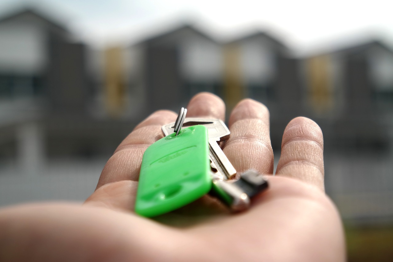 Open Left Hand With Key on Palm Directed Towards Houses