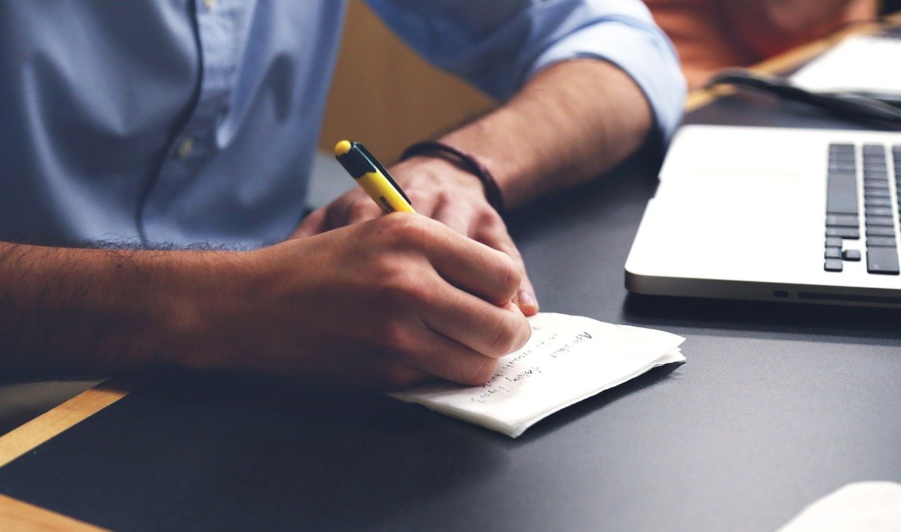 Partial Shot of a Man Writing on Paper Laid on Desk