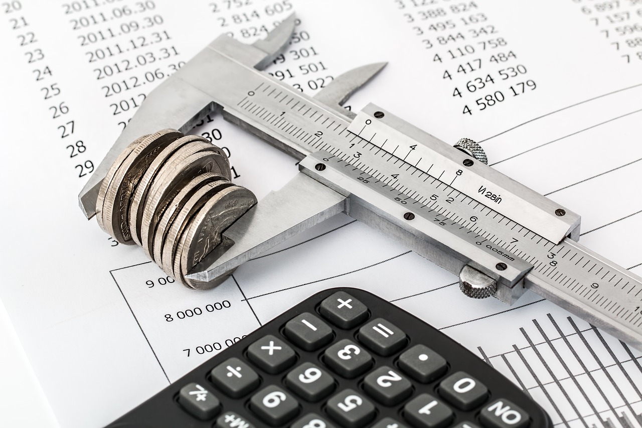 Caliper With Coins in Between with a Calculator in the Foreground and Financial Report in the Background